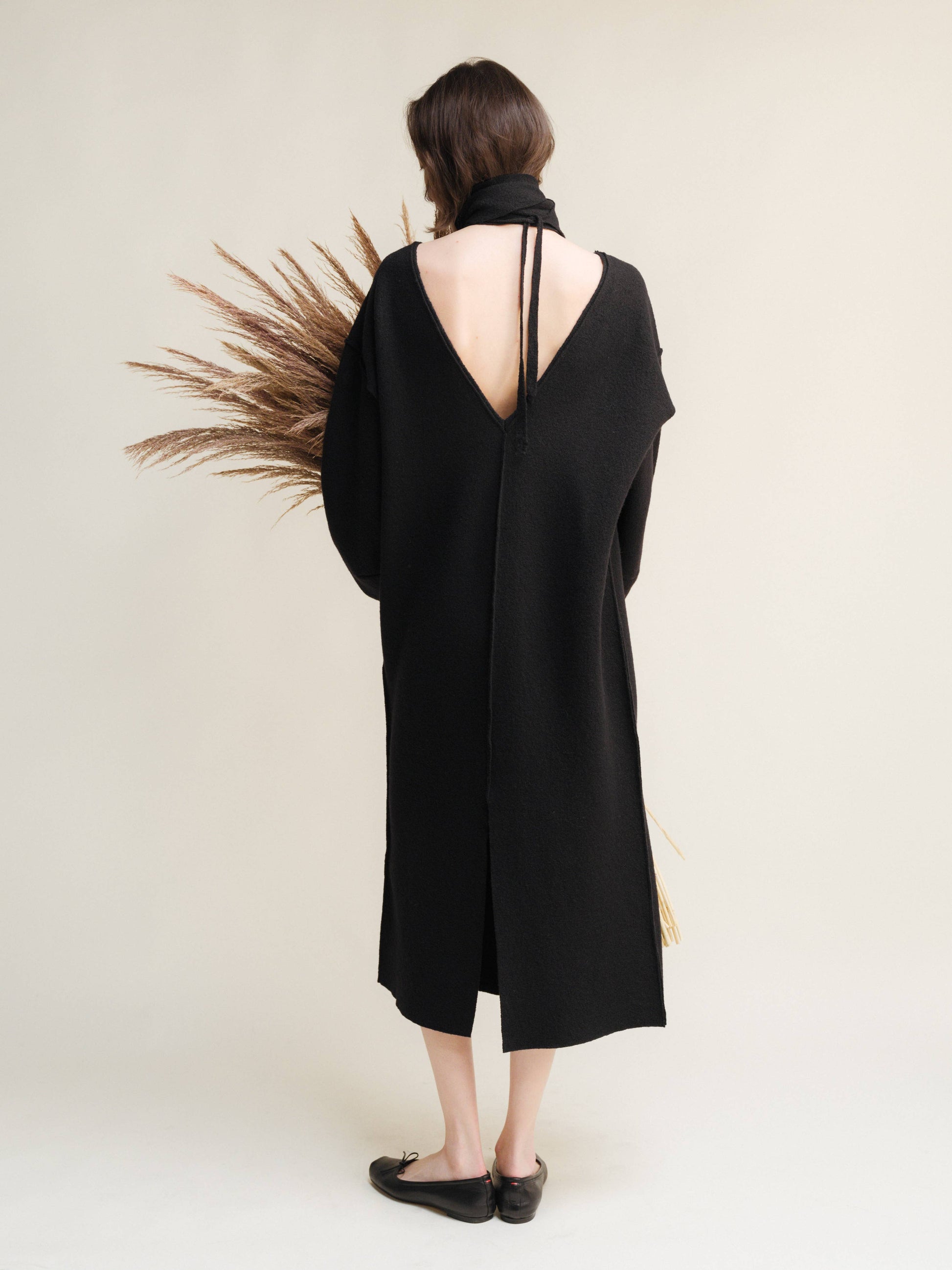 Person wearing a black dress with a deep back cutout, standing against a plain background.