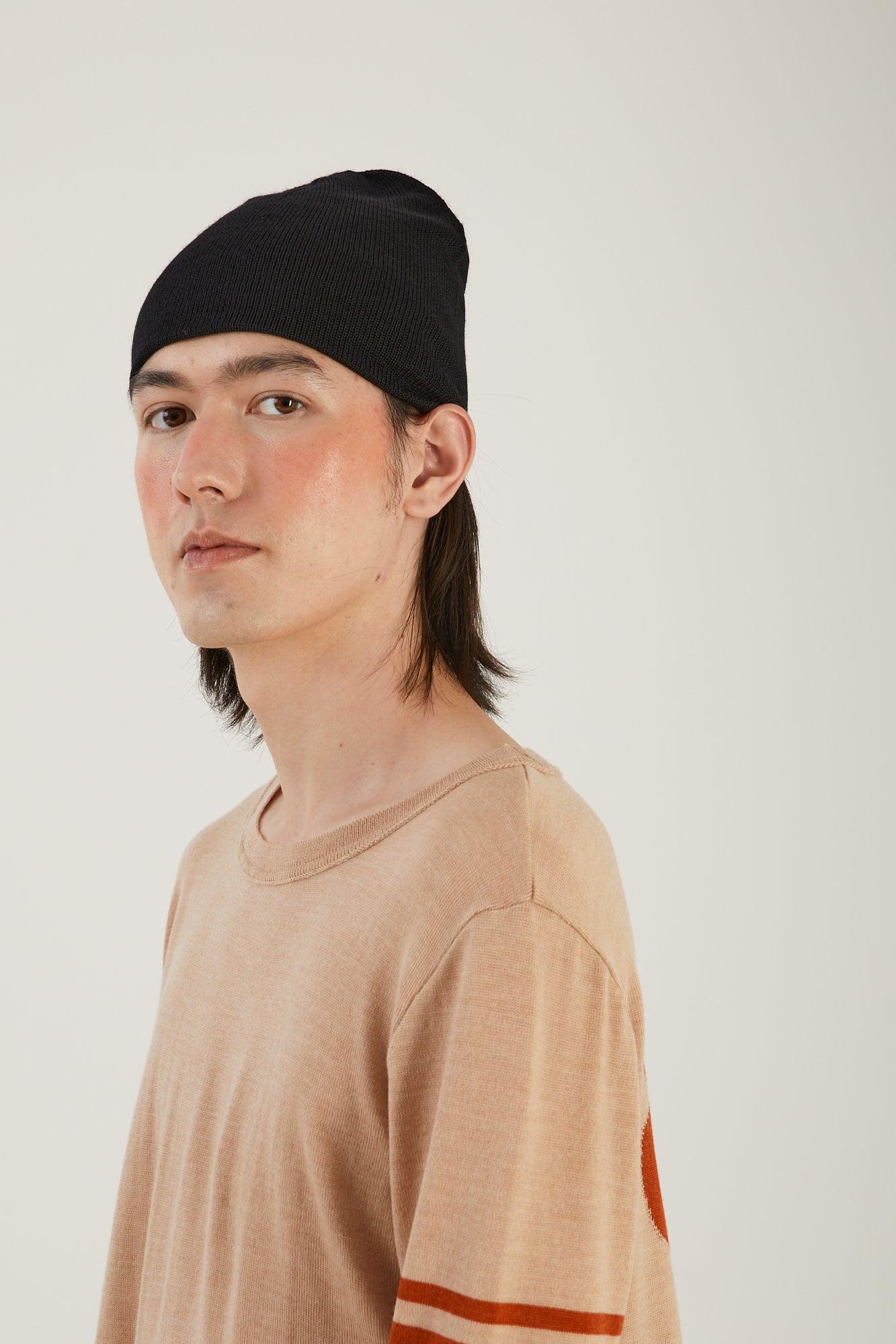 A person visible from the waist up looking into the camera wearing a merino wool jumper and a black merino wool beanie