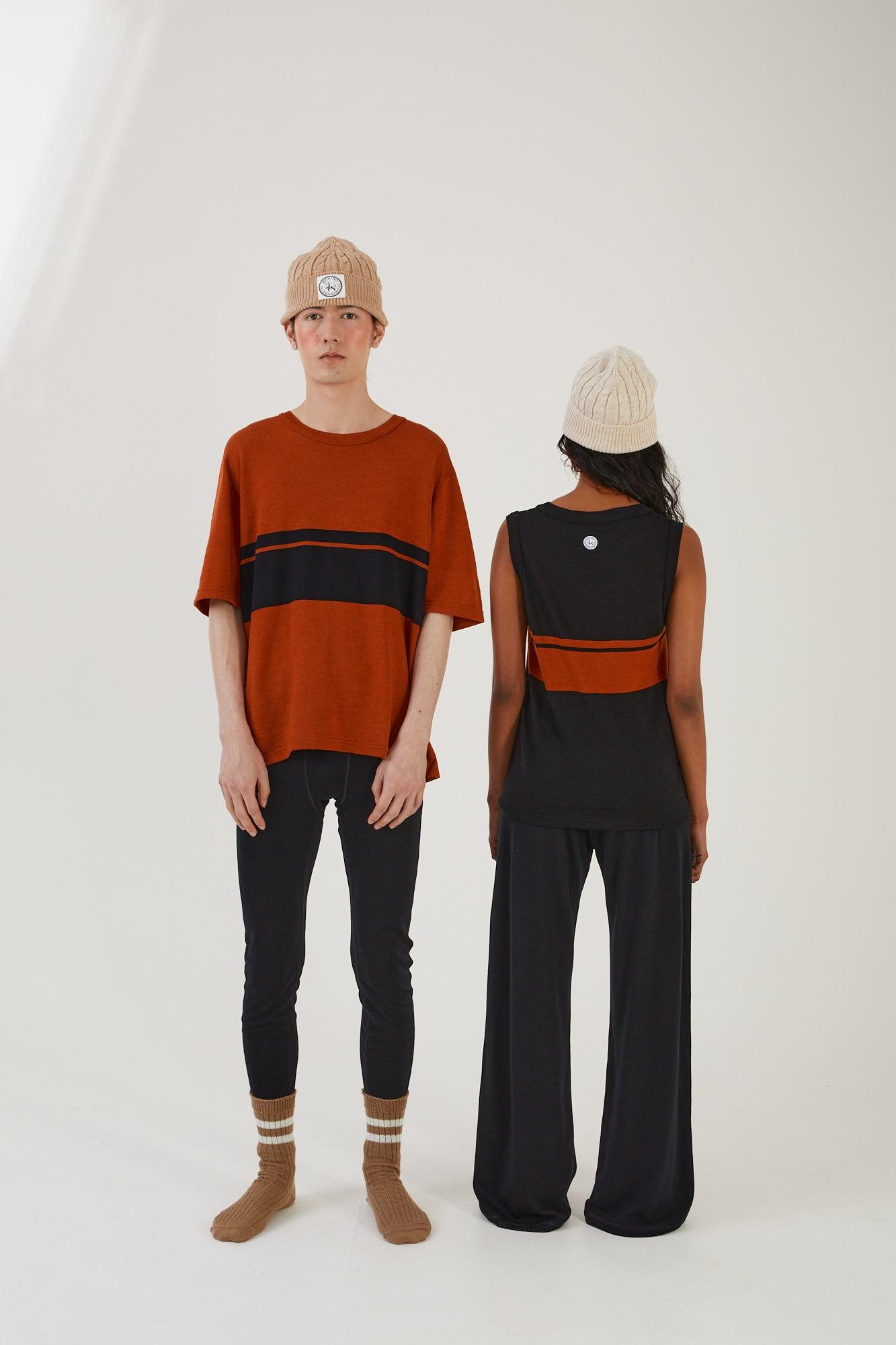 A person wearing merino wool socks, merino wool leggings, merino wool striped t-shirt and a merino wool beanie standing next to someone wearing merino wool track pants, a merino wool striped vest and a merino wool beanie
