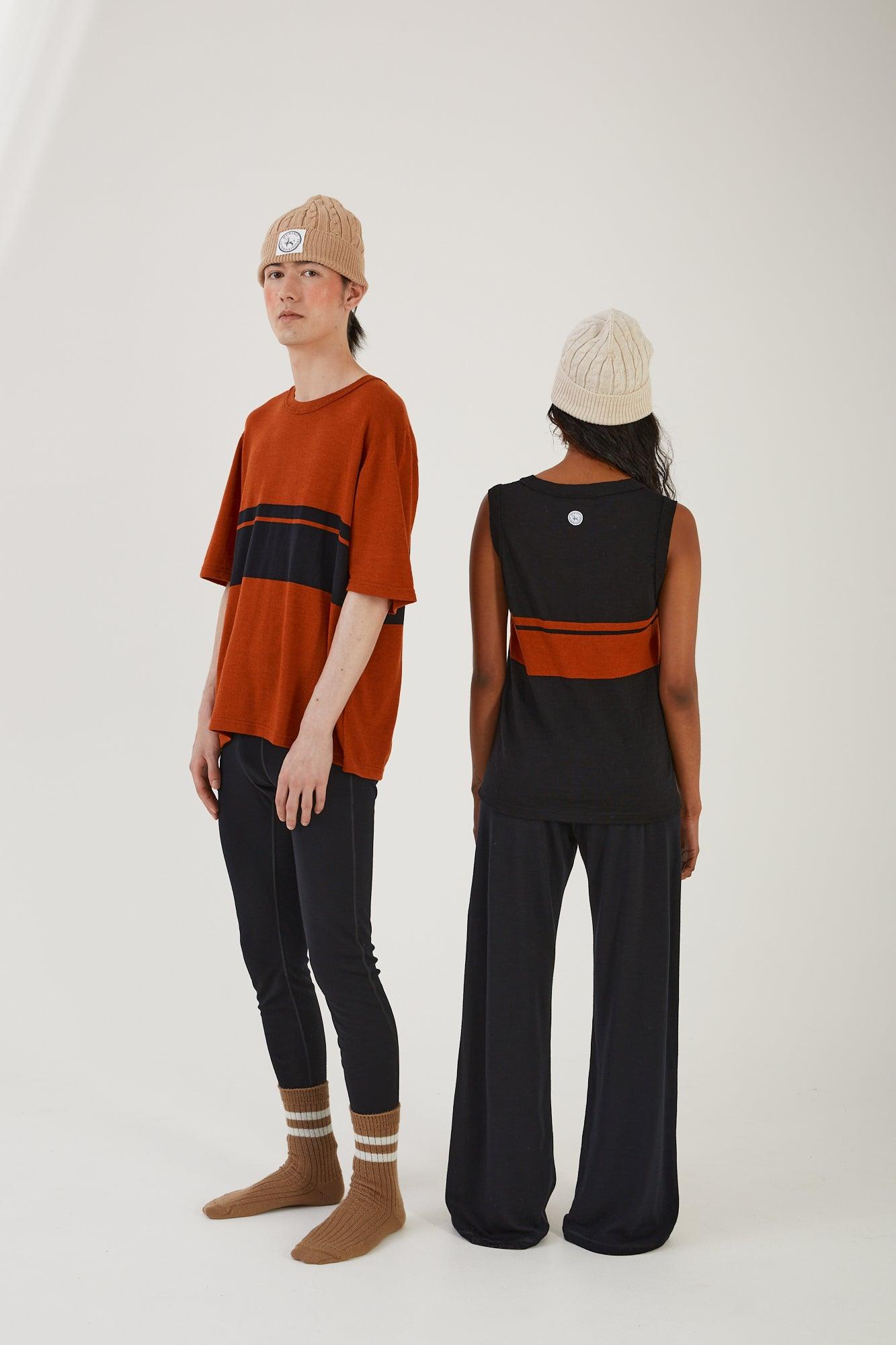 A person wearing merino wool socks, merino wool leggings, a merino wool t-shirt and a merino wool beanie standing next to another person wearing merino wool track pants, a merino wool vest and merino wool beanie