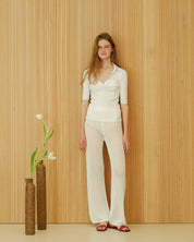 Person in a white outfit standing against a wooden panelled wall with two vases.