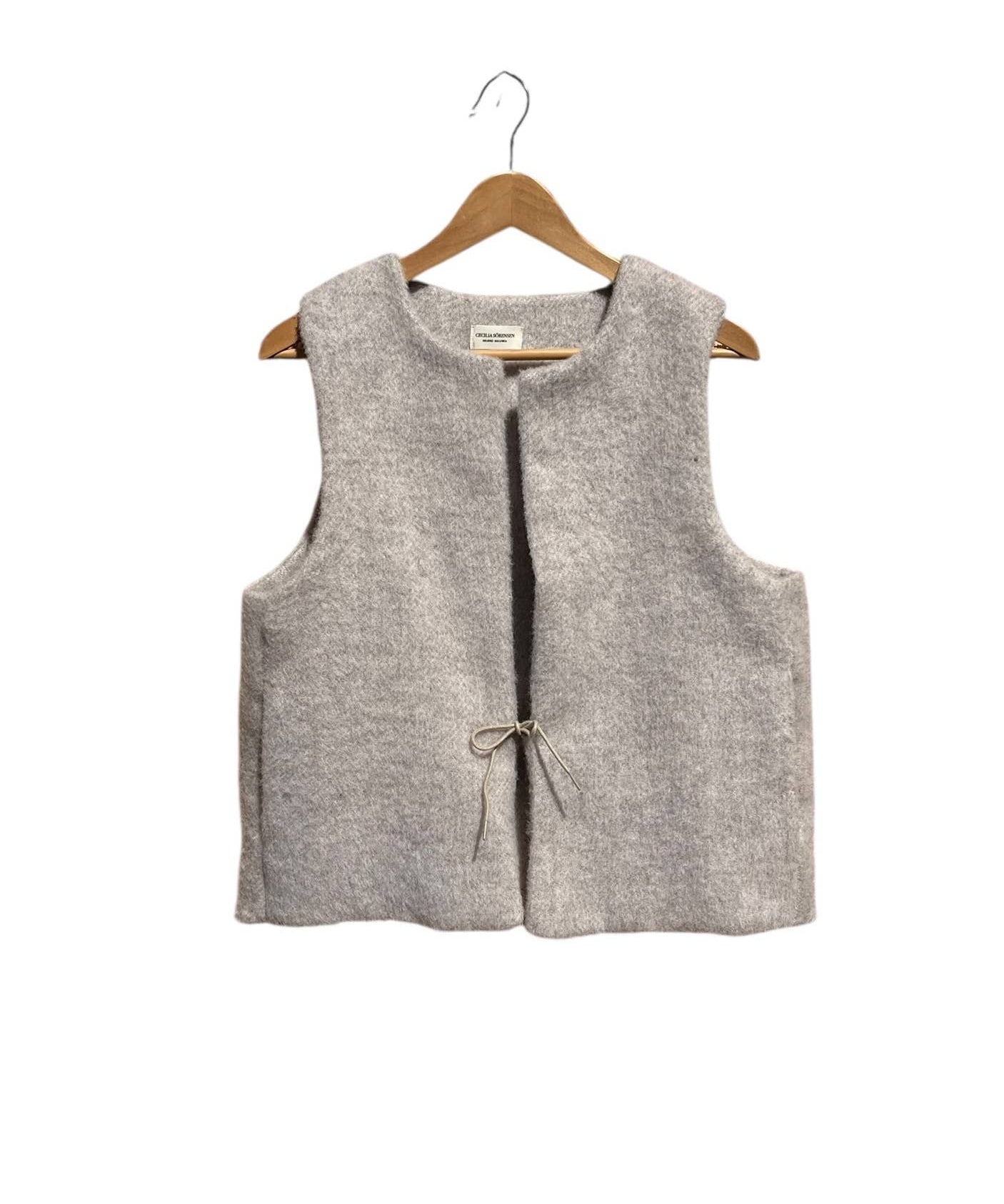Beige sleeveless vest on a wooden hanger against a white background