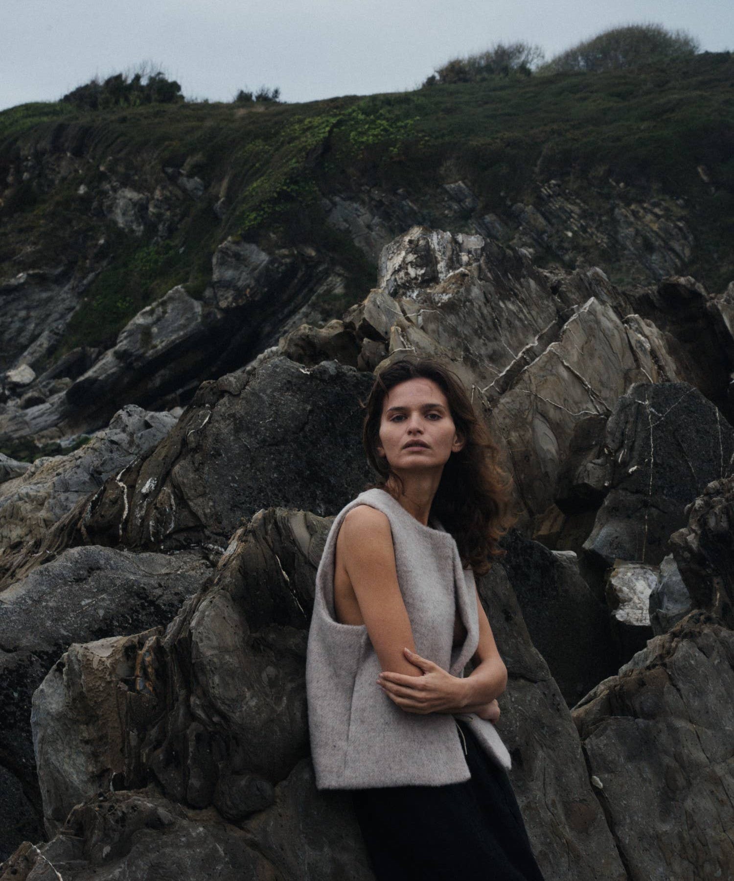 Woman standing on rocky terrain with a neutral expression wearing a beige wool vest