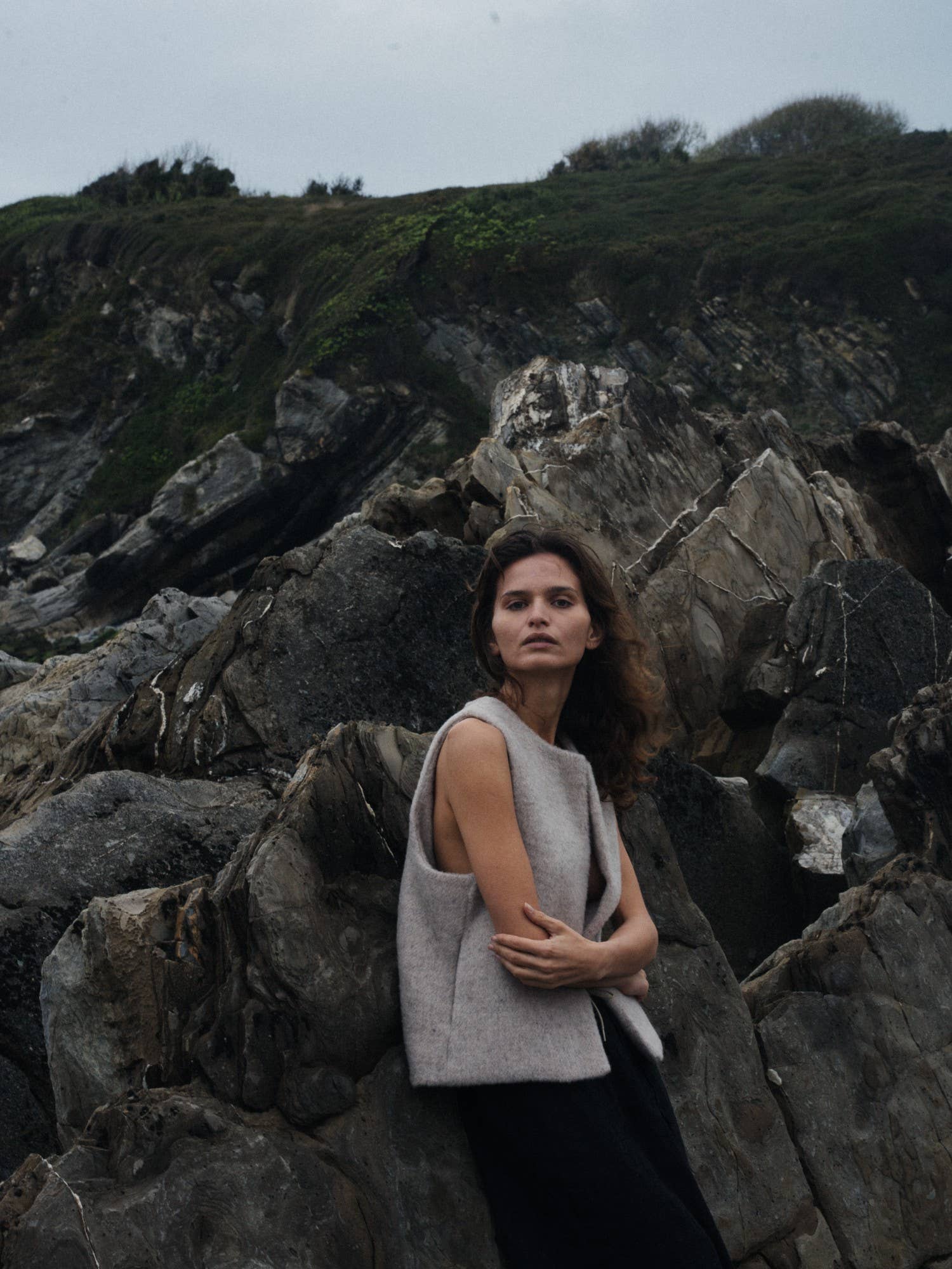 Woman standing on rocky terrain with a neutral expression wearing a beige wool vest