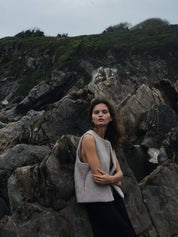 Woman standing on rocky terrain with a neutral expression wearing a beige wool vest