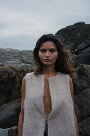 Woman wearing a sleeveless beige vest standing against a rocky background