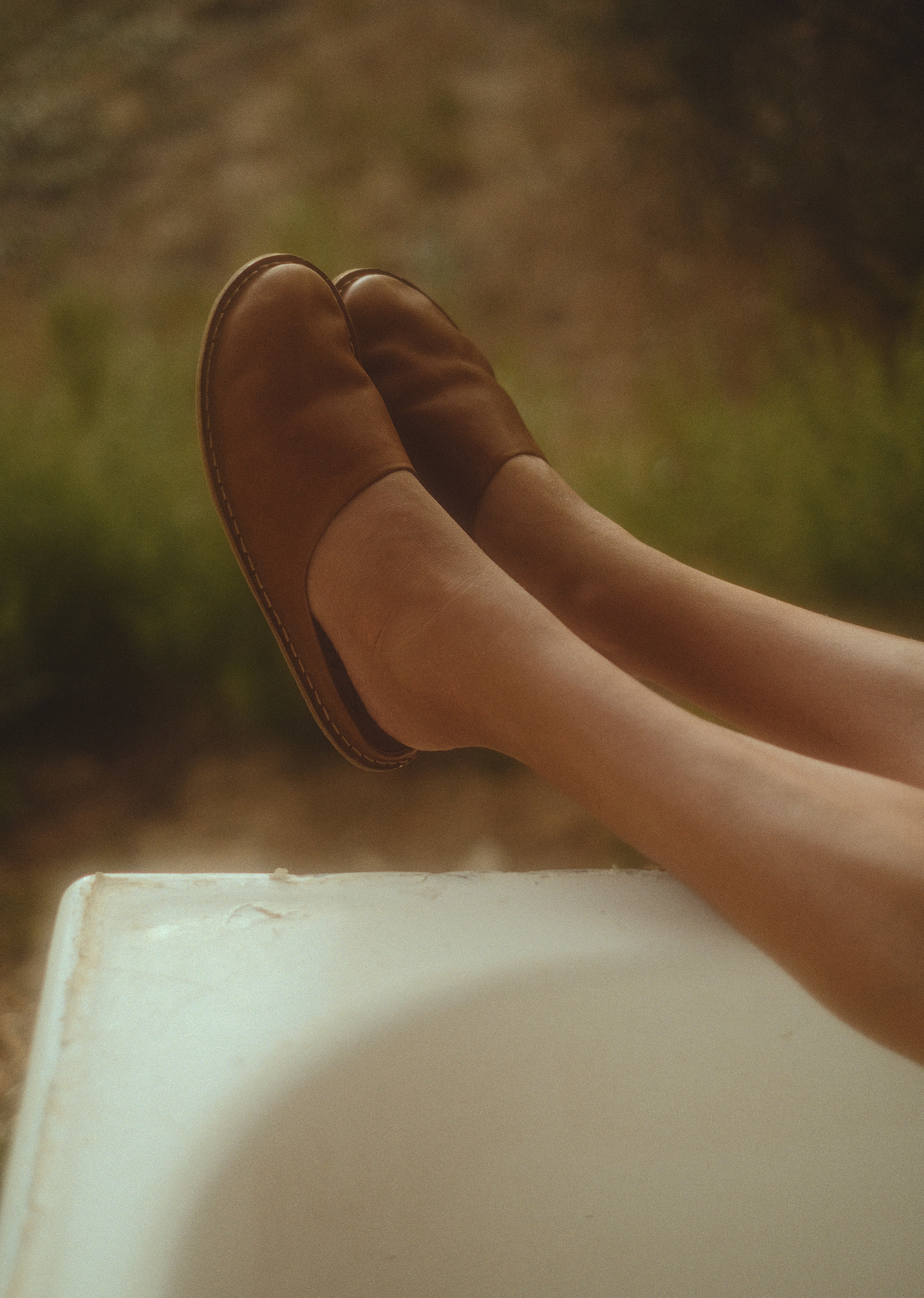 Brown leather shoes on a person's feet with a blurred natural background