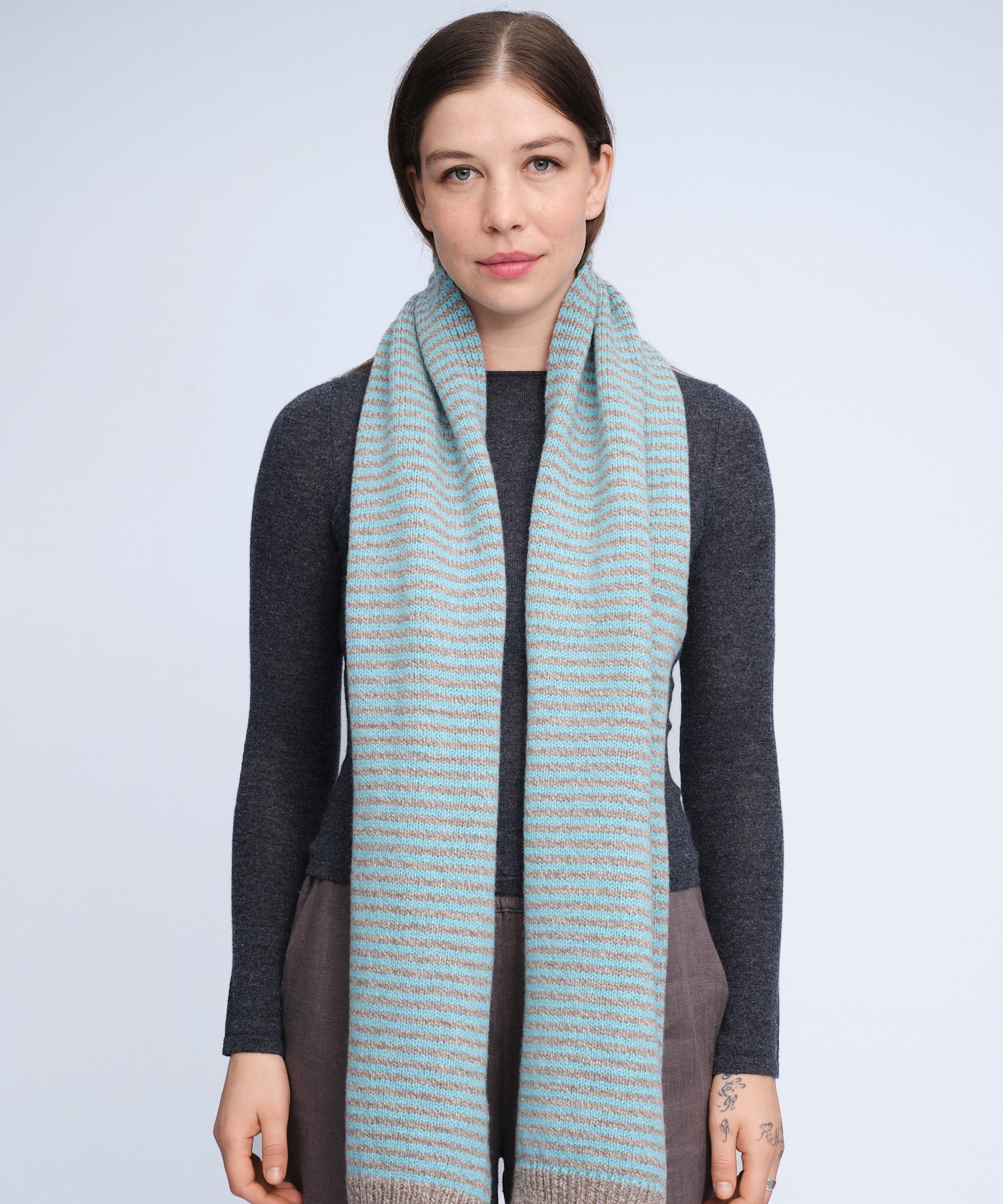 Woman wearing a long, light blue scarf with thin stripes on a plain background