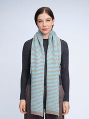 Woman wearing a long, light blue scarf with thin stripes on a plain background