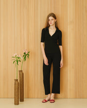 Person in a black outfit standing next to two vases with flowers against a wooden panelled wall.