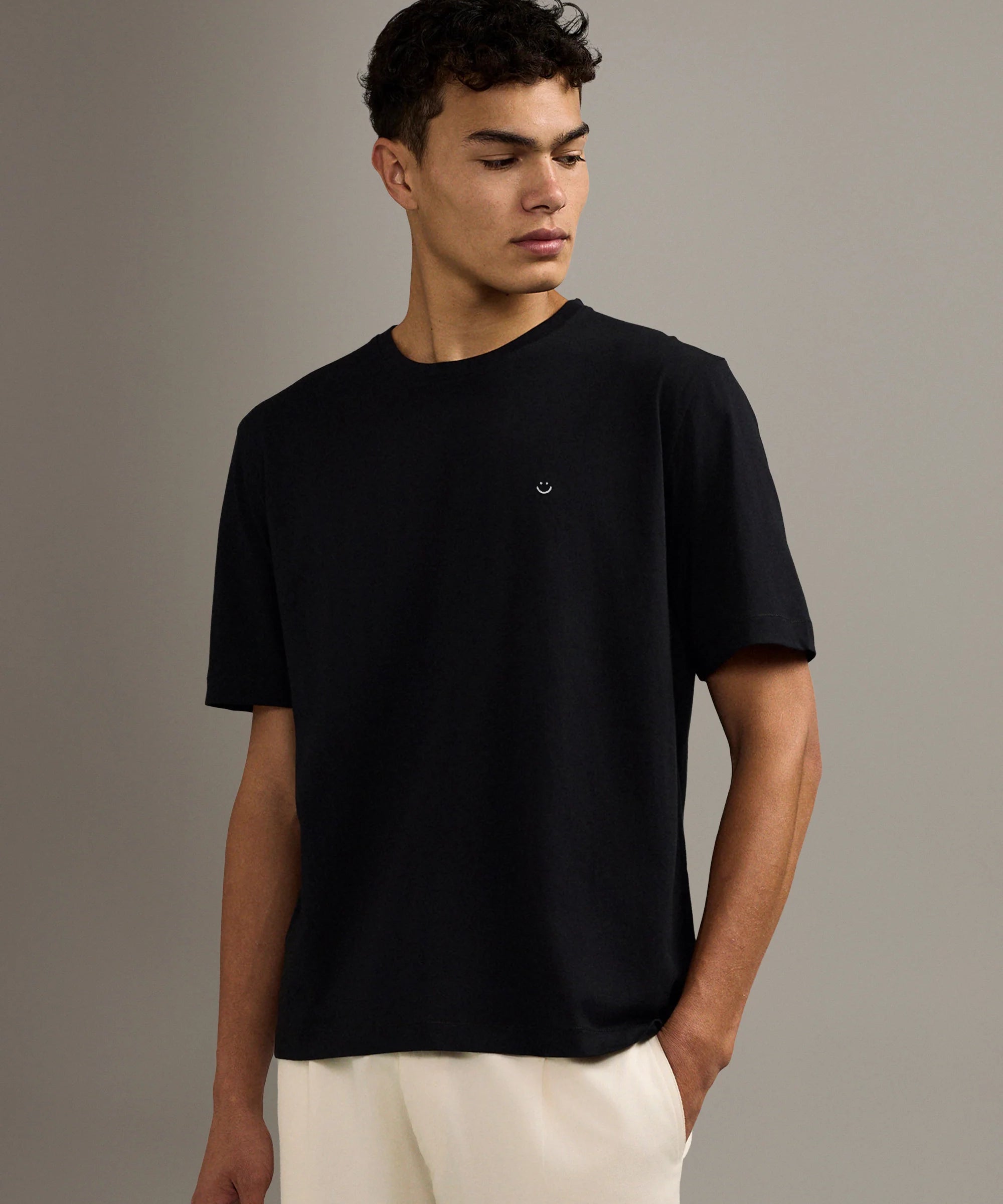 Man wearing a black t-shirt and white pants against a gray background