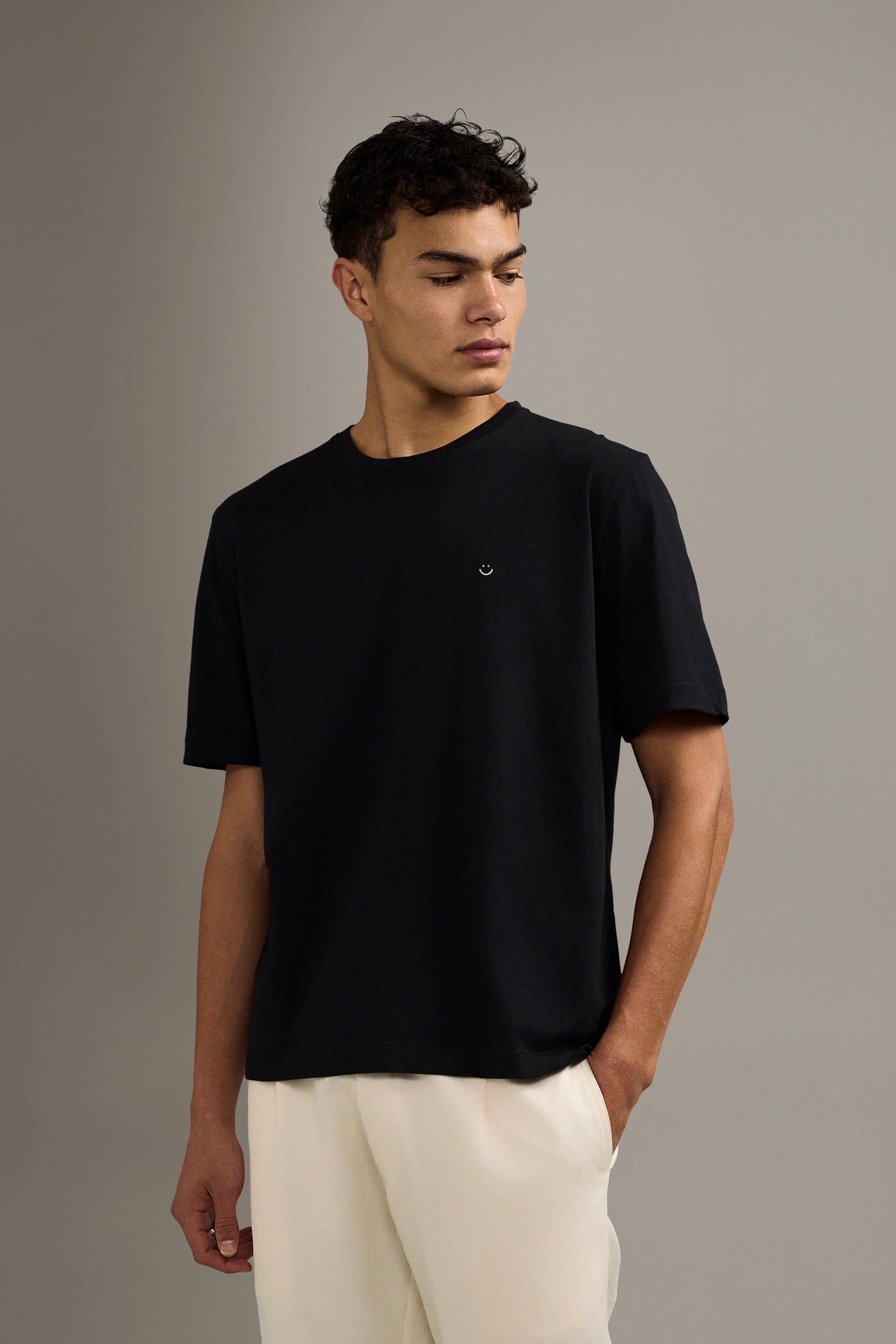 Man wearing a black t-shirt and white pants against a gray background