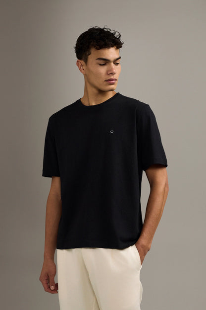 Man wearing a black t-shirt and white pants against a gray background