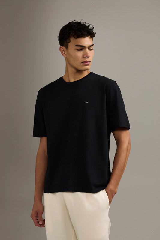 Man wearing a black t-shirt and white pants against a gray background