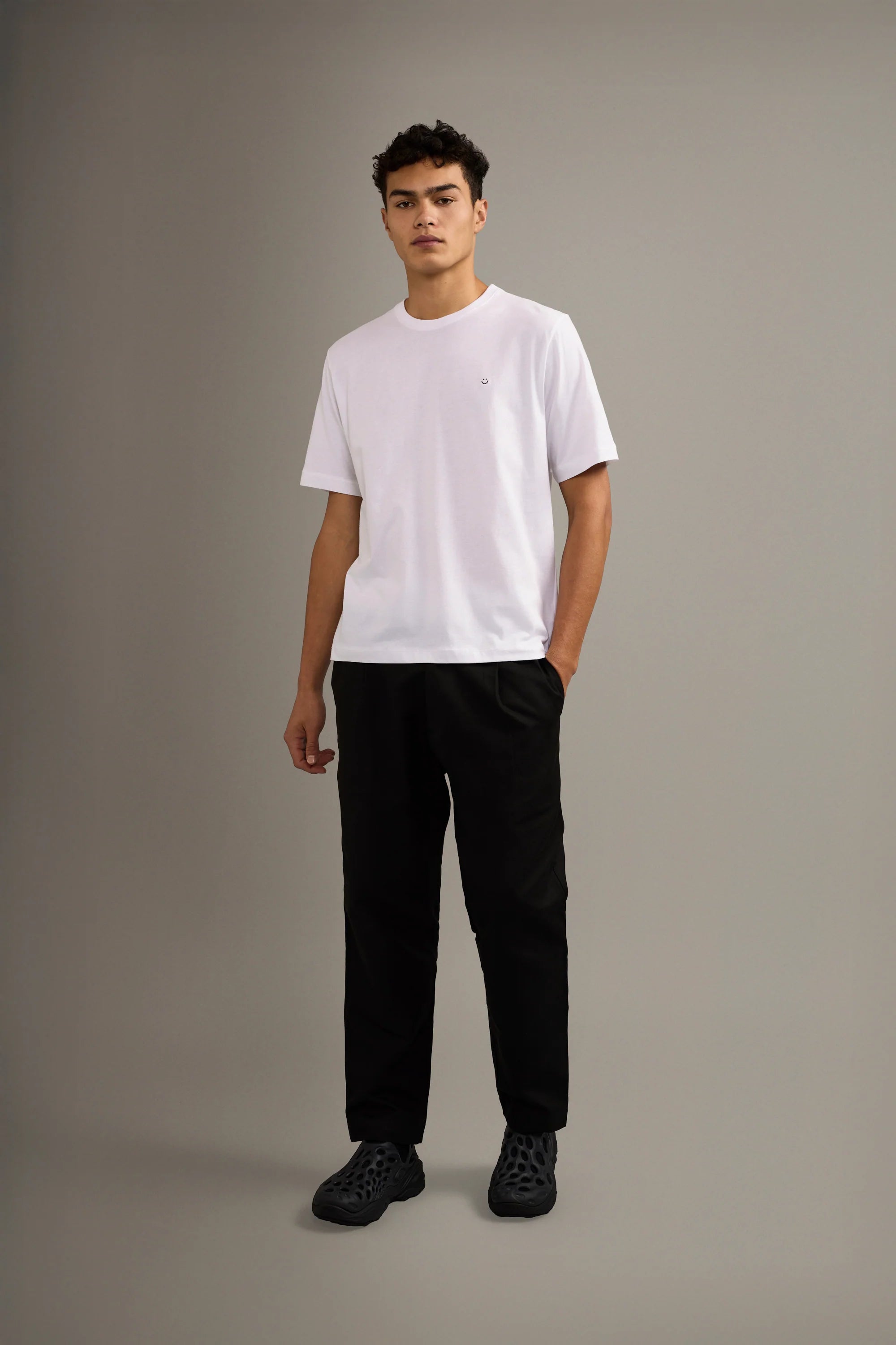 Person wearing a white t-shirt and black pants on a gray background