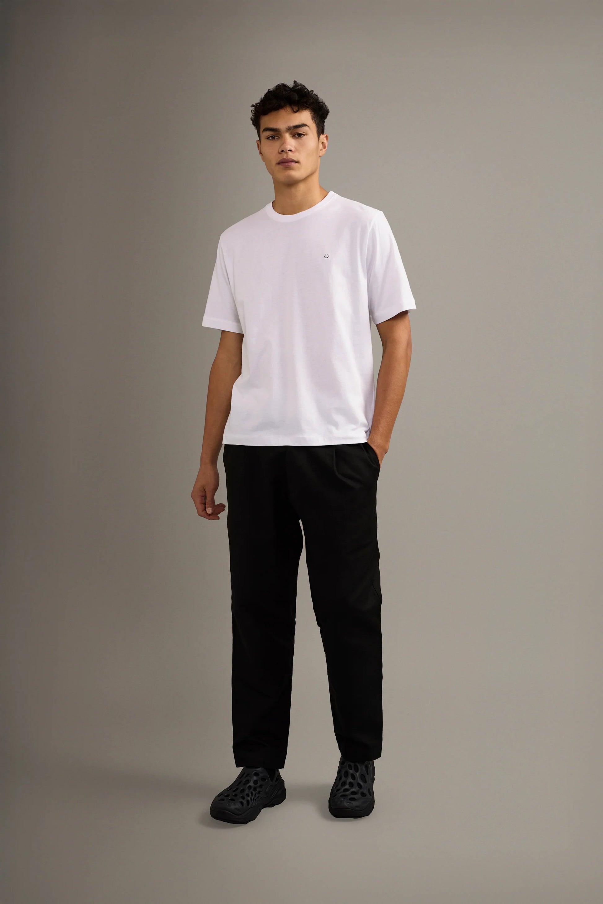 Person wearing a white t-shirt and black pants on a gray background