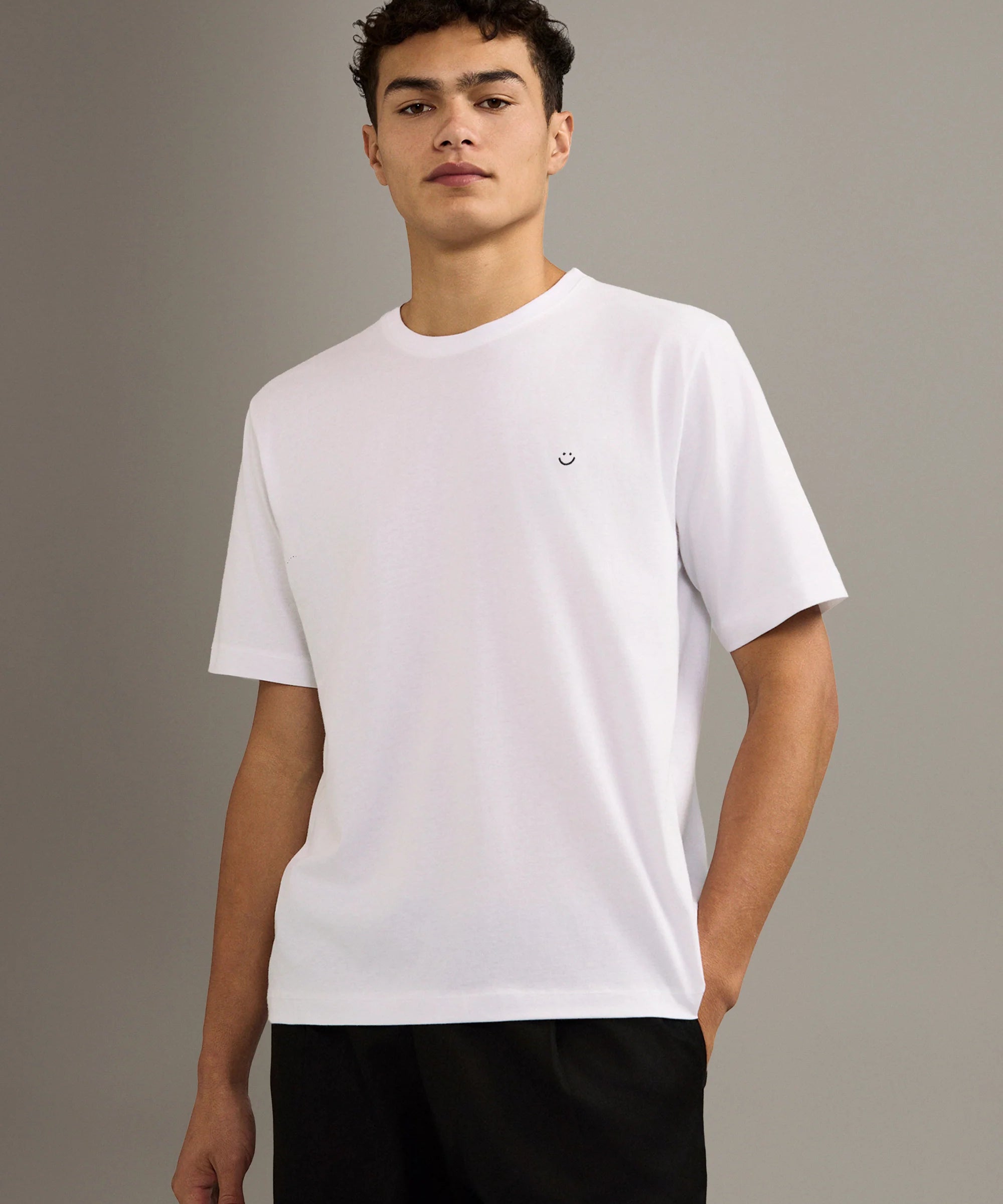 Person wearing a white t-shirt with a small smiley face logo on a gray background