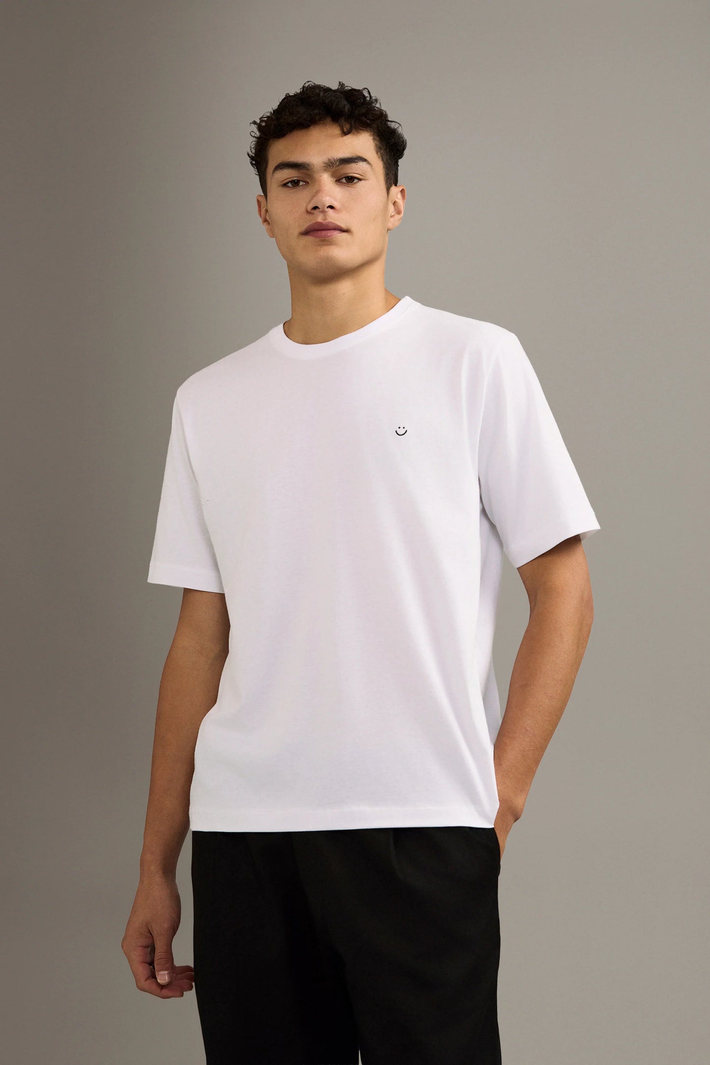 Person wearing a white t-shirt with a small smiley face logo on a gray background