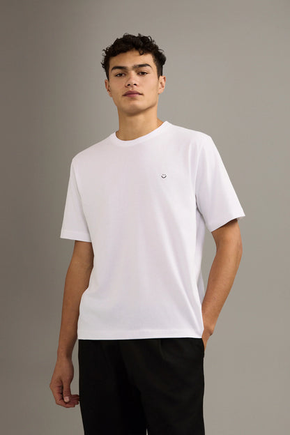 Person wearing a white t-shirt with a small smiley face logo on a gray background