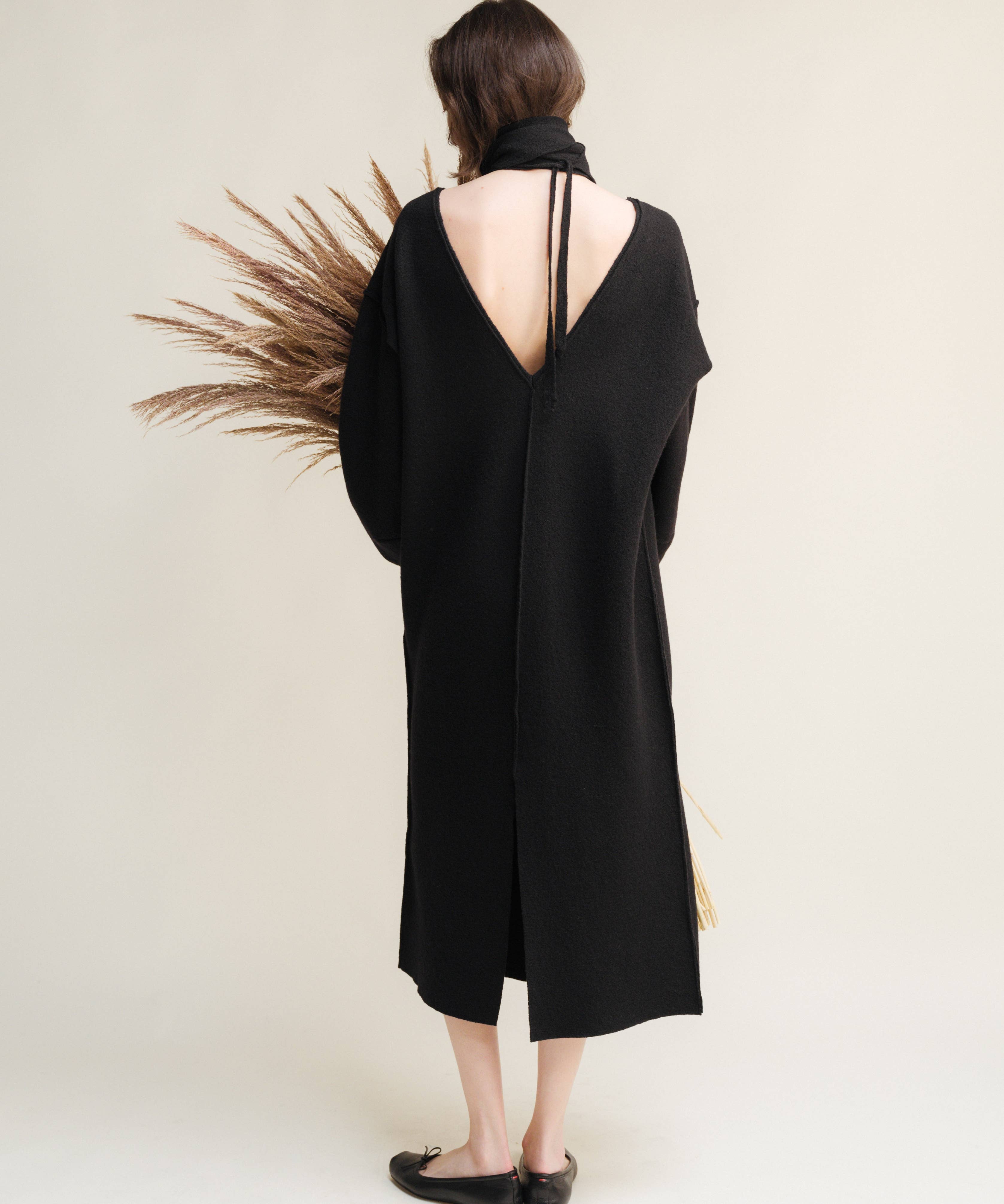 Person wearing a black dress with a deep back cutout, standing against a plain background.