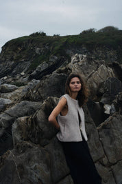 Woman standing on rocky terrain with a mountainous background in a beige vest