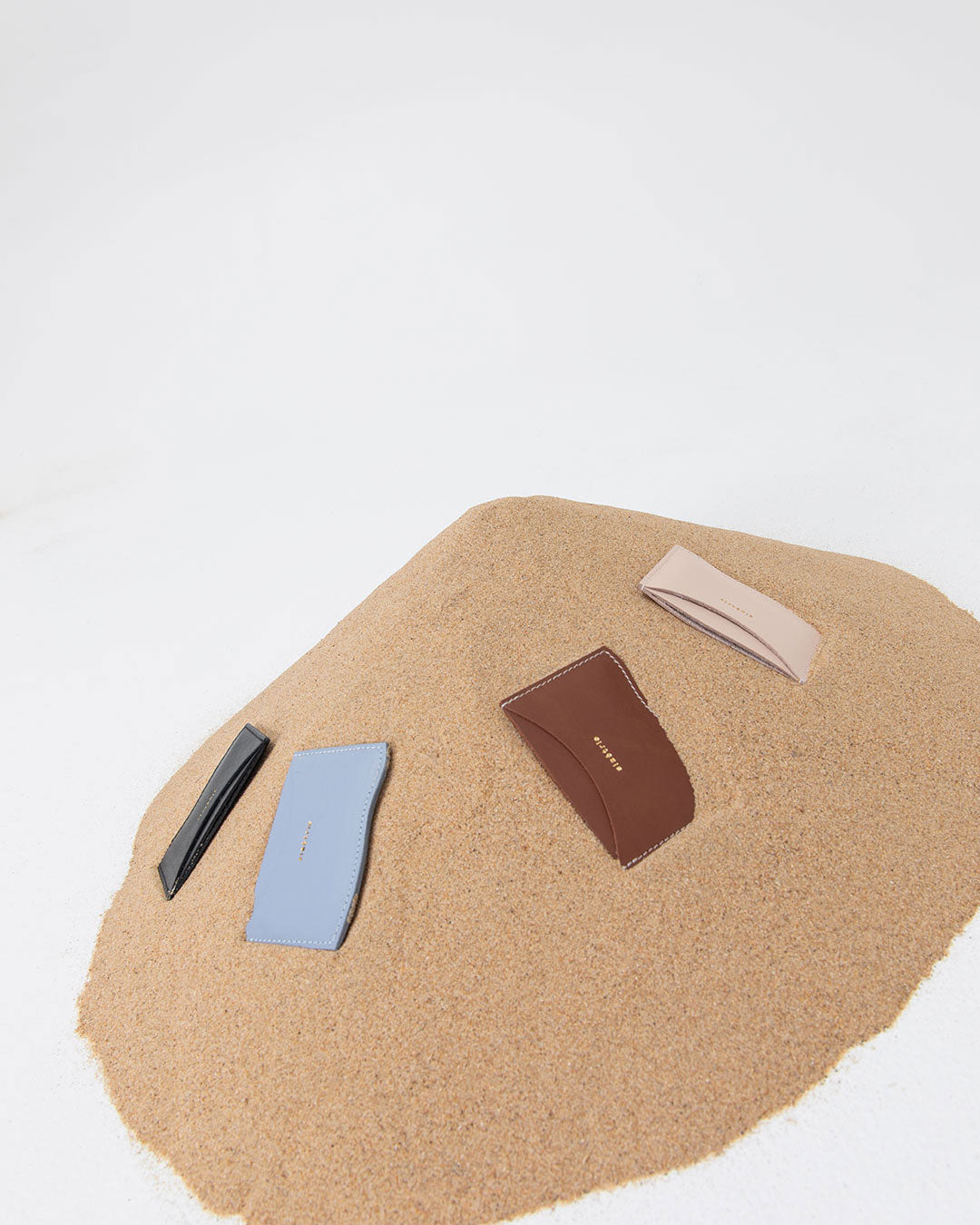 Four card wallets on a pile of sand on a white background