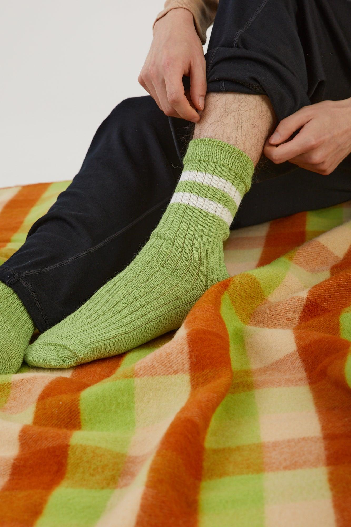 Close up of a person sitting on a wool blanket wearing merino wool track pants, putting on a merino wool sock