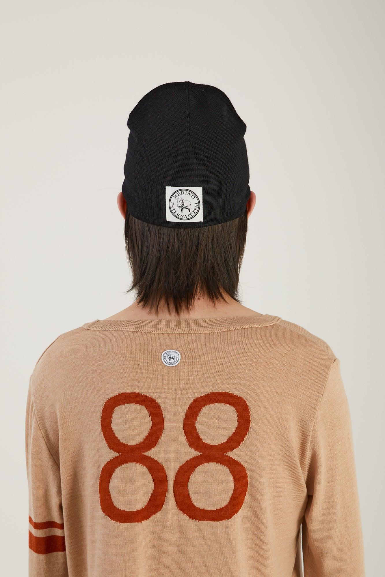 The back of a person visible from the waist up wearing a merino wool jumper with 88 knitted into the back and a black merino wool beanie