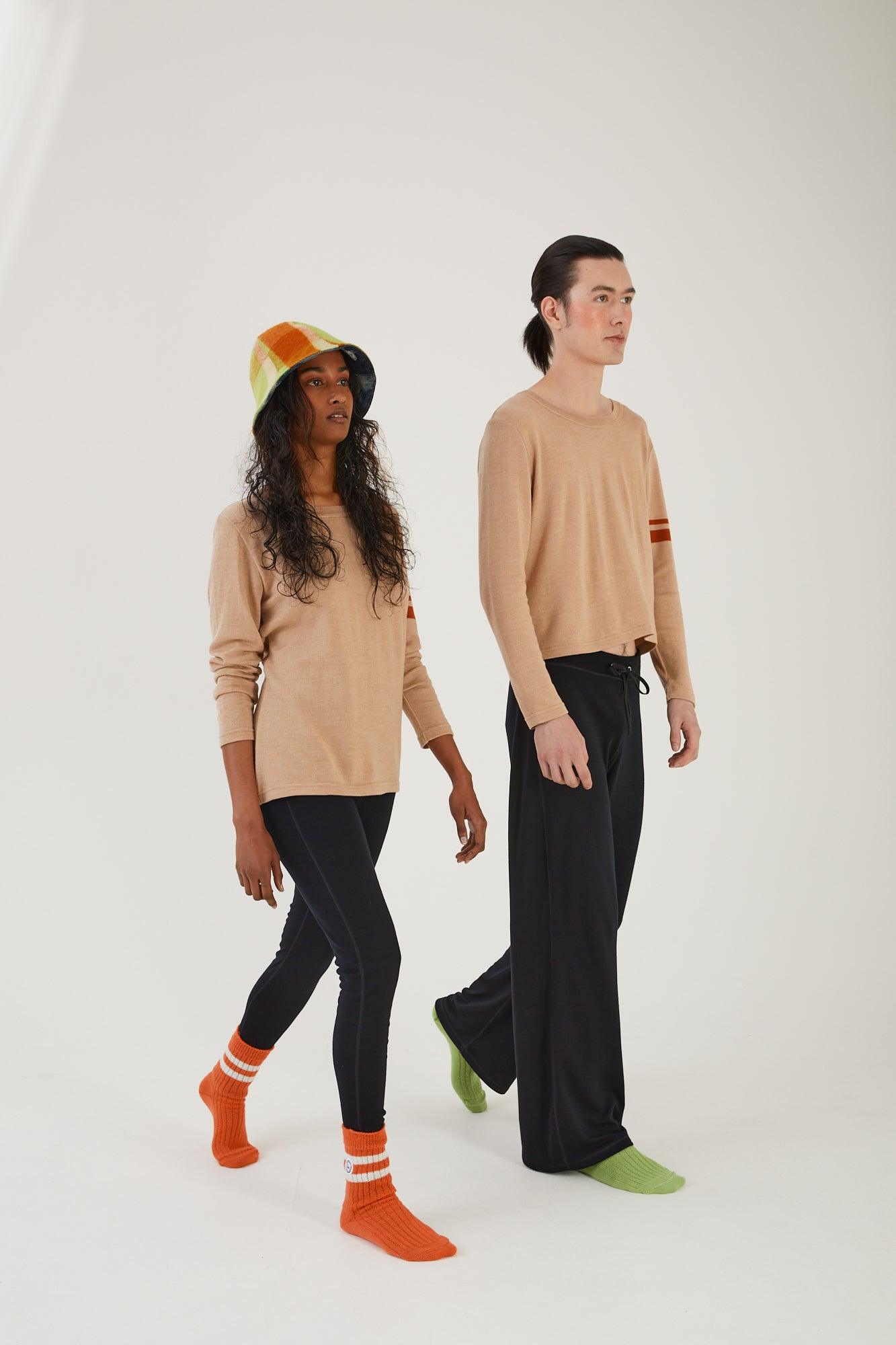 A person walking wearing merino wool socks, merino wool leggings, a merino wool jumper and an upcycled wool blanket hat next to another person wearing merino wool socks, merino wool track pants and a merino wool sweater