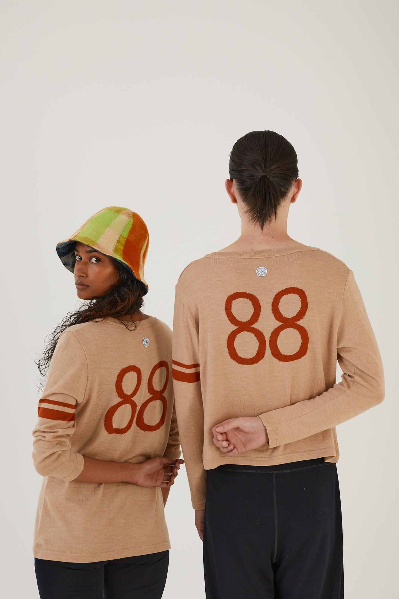 Two people wearing merino wool jumpers with their backs to the camera, the person on the left looking over their shoulder wearing an upcycled wool blanket hat