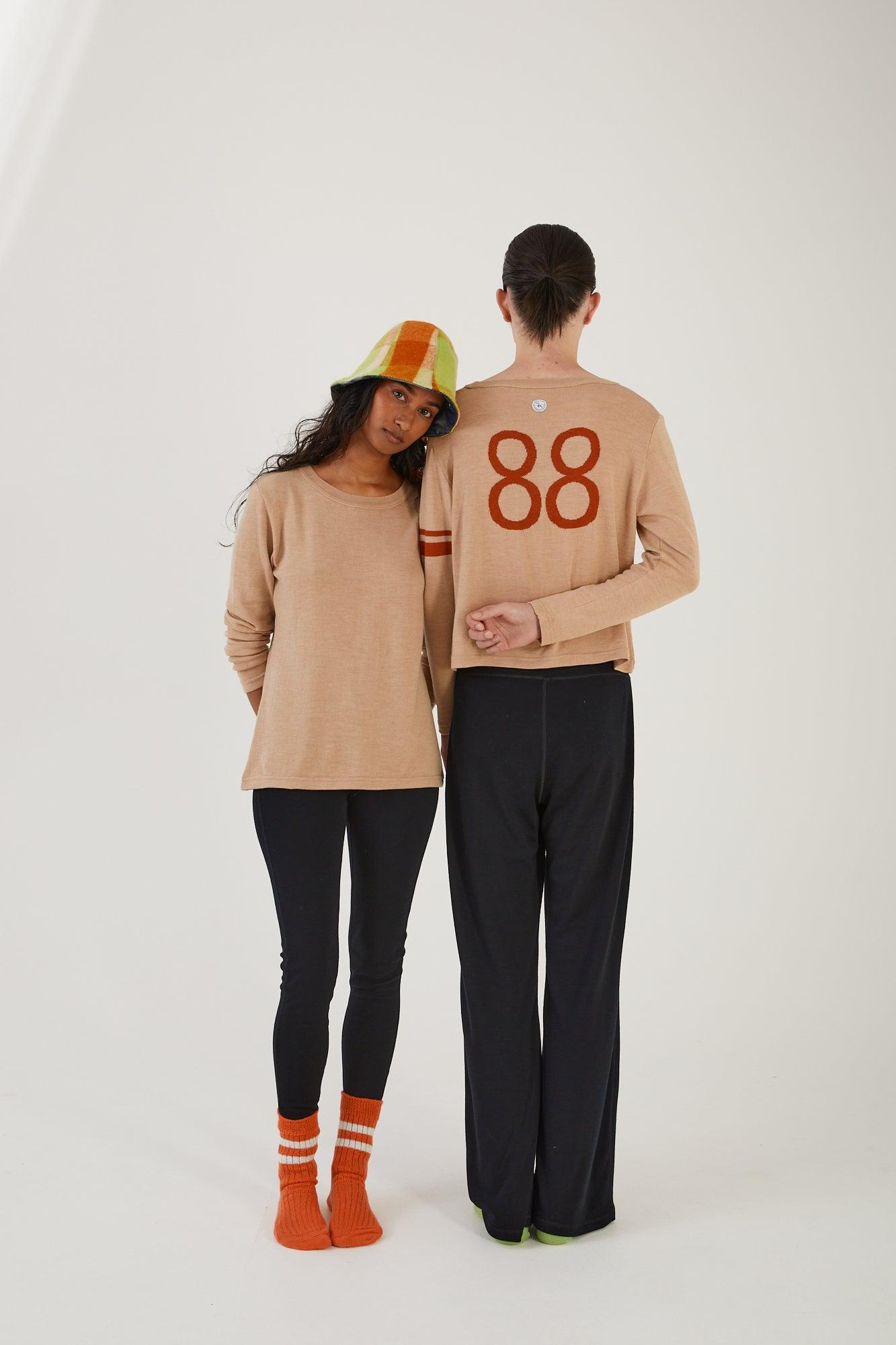 A person wearing merino wool socks, merino wool leggings, a merino wool jumper and an upcycled wool blanket hat leaning on a person with their back to the camera wearing merino wool socks, merino wool track pants and a merino wool sweater