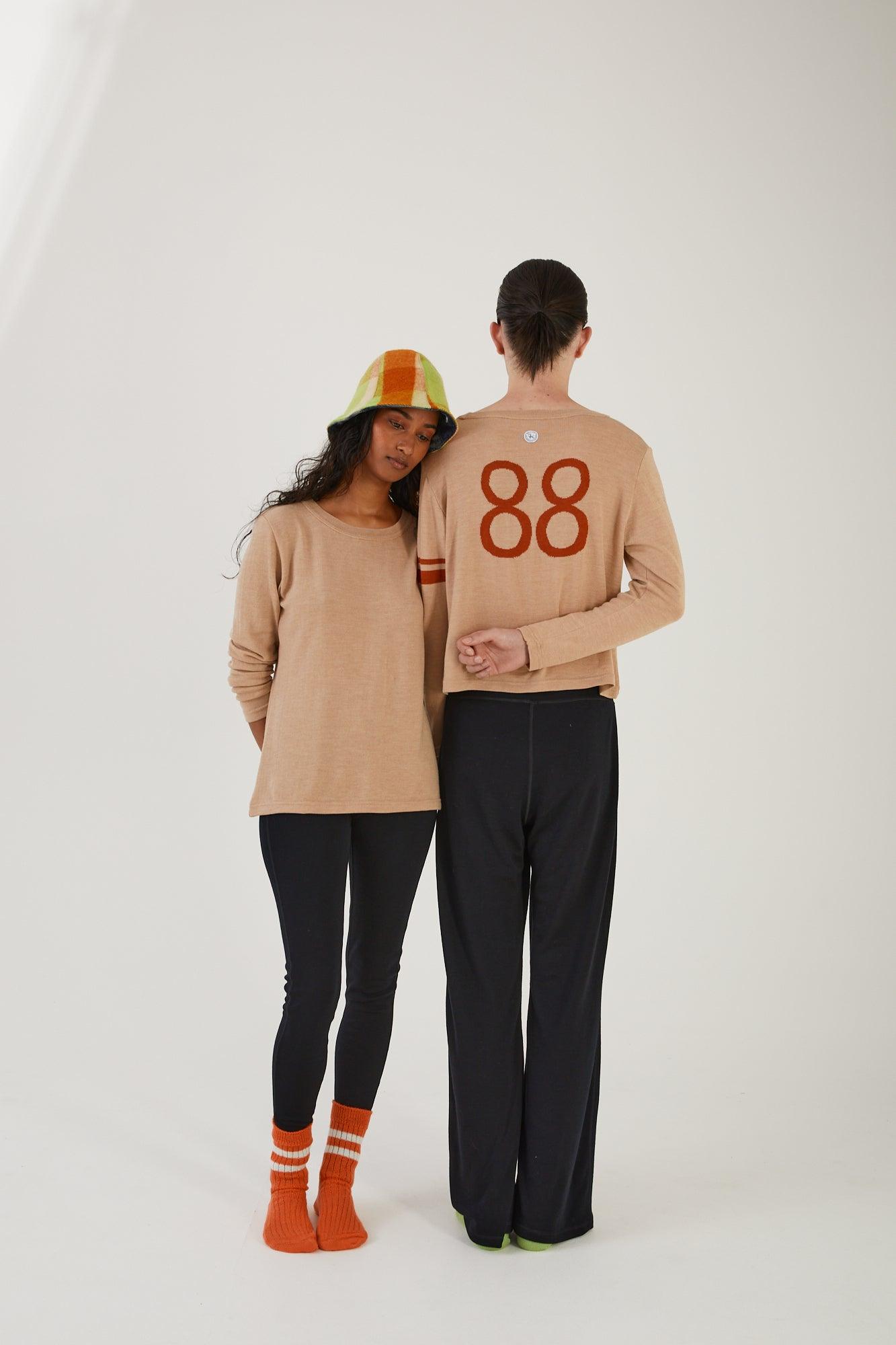 A person wearing merino wool socks, merino wool leggings, a merino wool sweater and an upcycled wool blanket hat leaning on someone wearing merino wool socks, merino wool track pants and a merino wool jumper