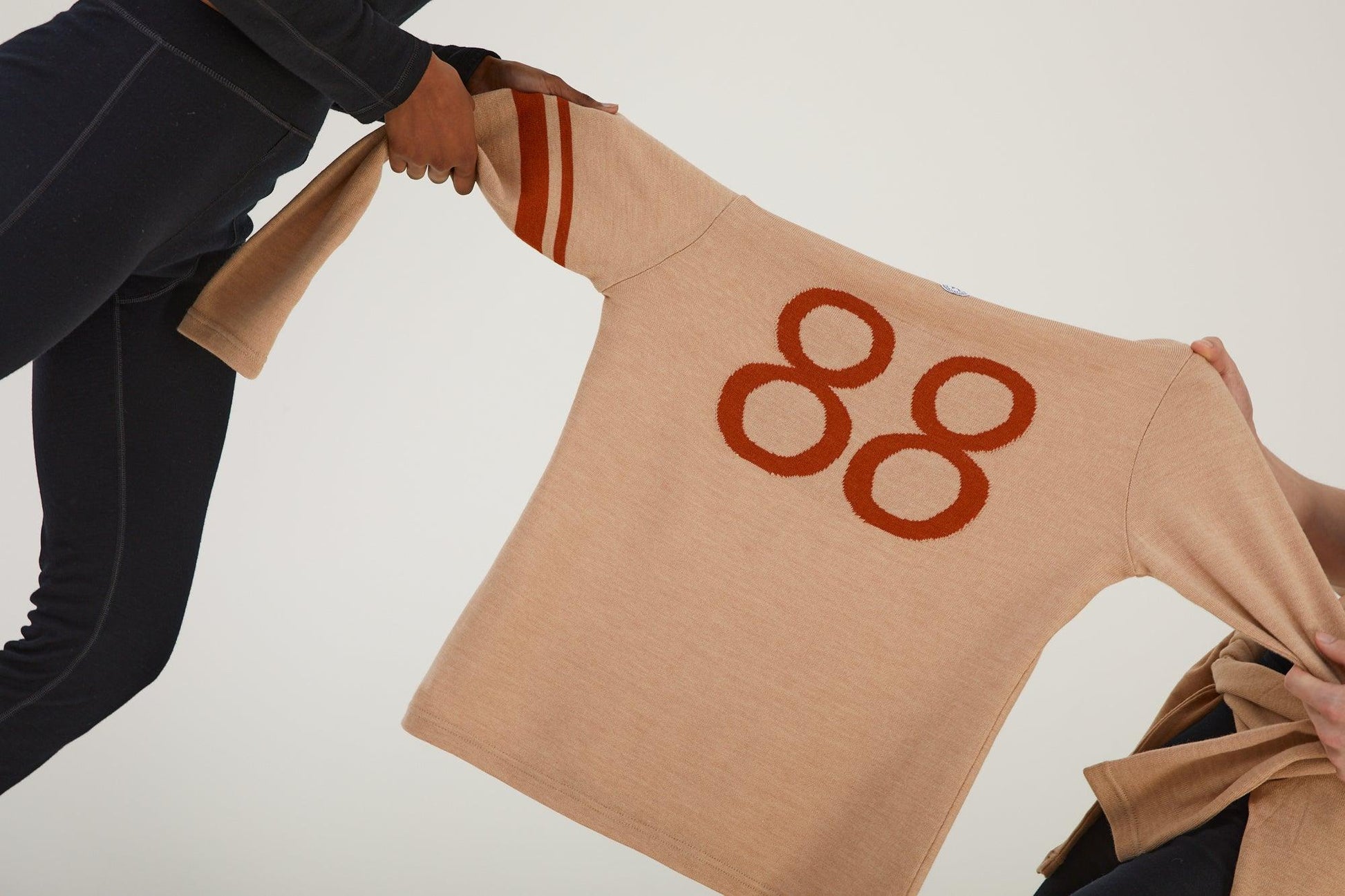 Close up of two people playing tug of war over a merino wool jumper whilst wearing merino wool clothing