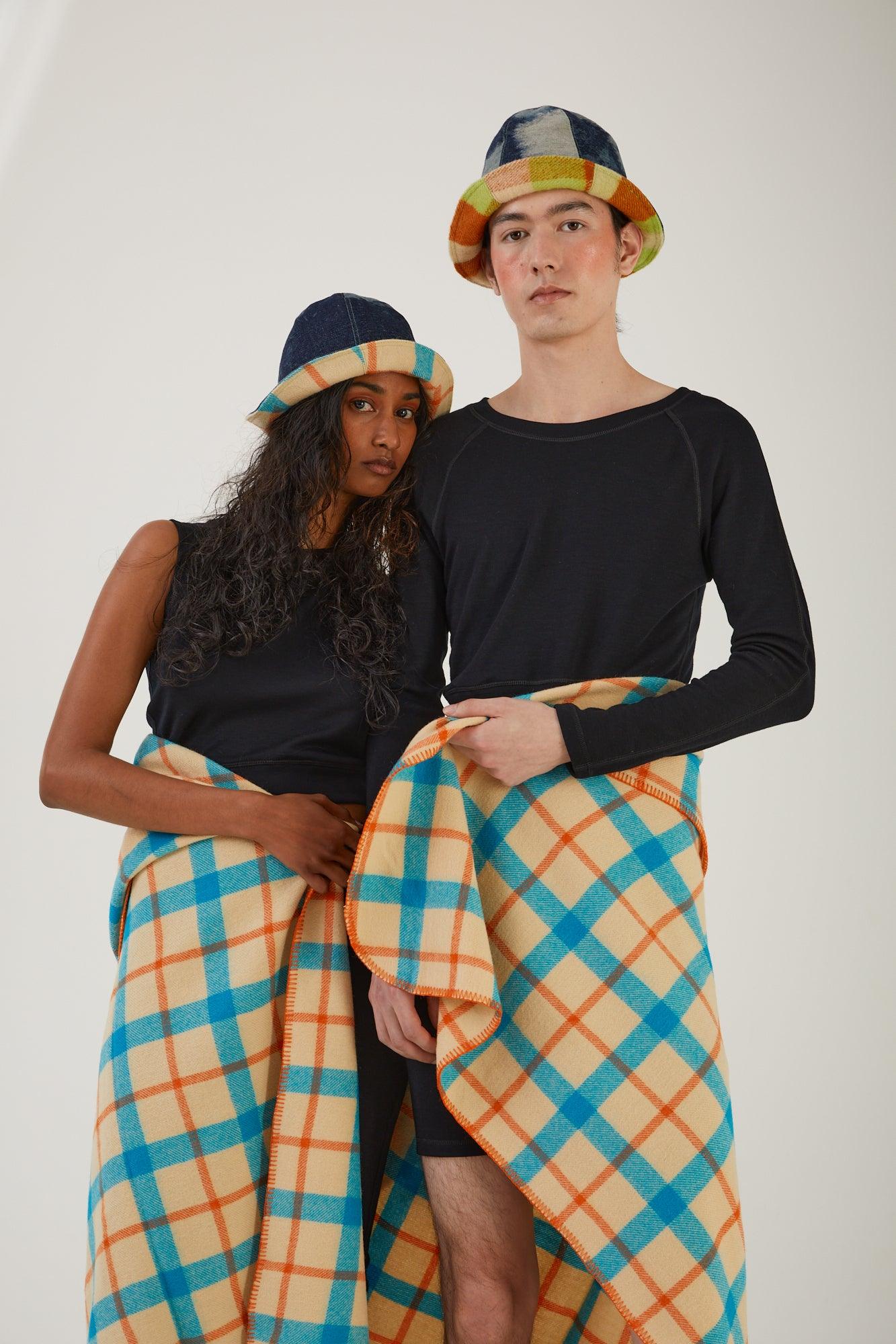 Two people standing together with a wool blanket wrapped around their waists wearing merino wool tops, merino wool bottoms and upcycled hats