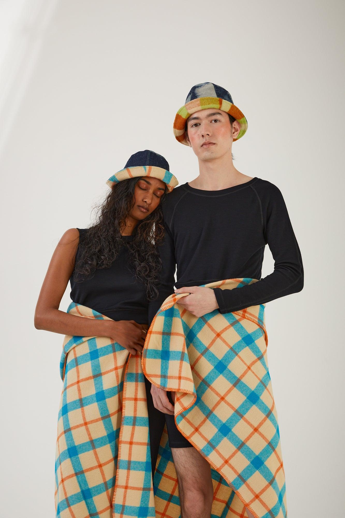 Two people standing wearing merino wool clothing and upcycled deadstock denim and wool blanket hats with a wool blanket wrapped around their waists 