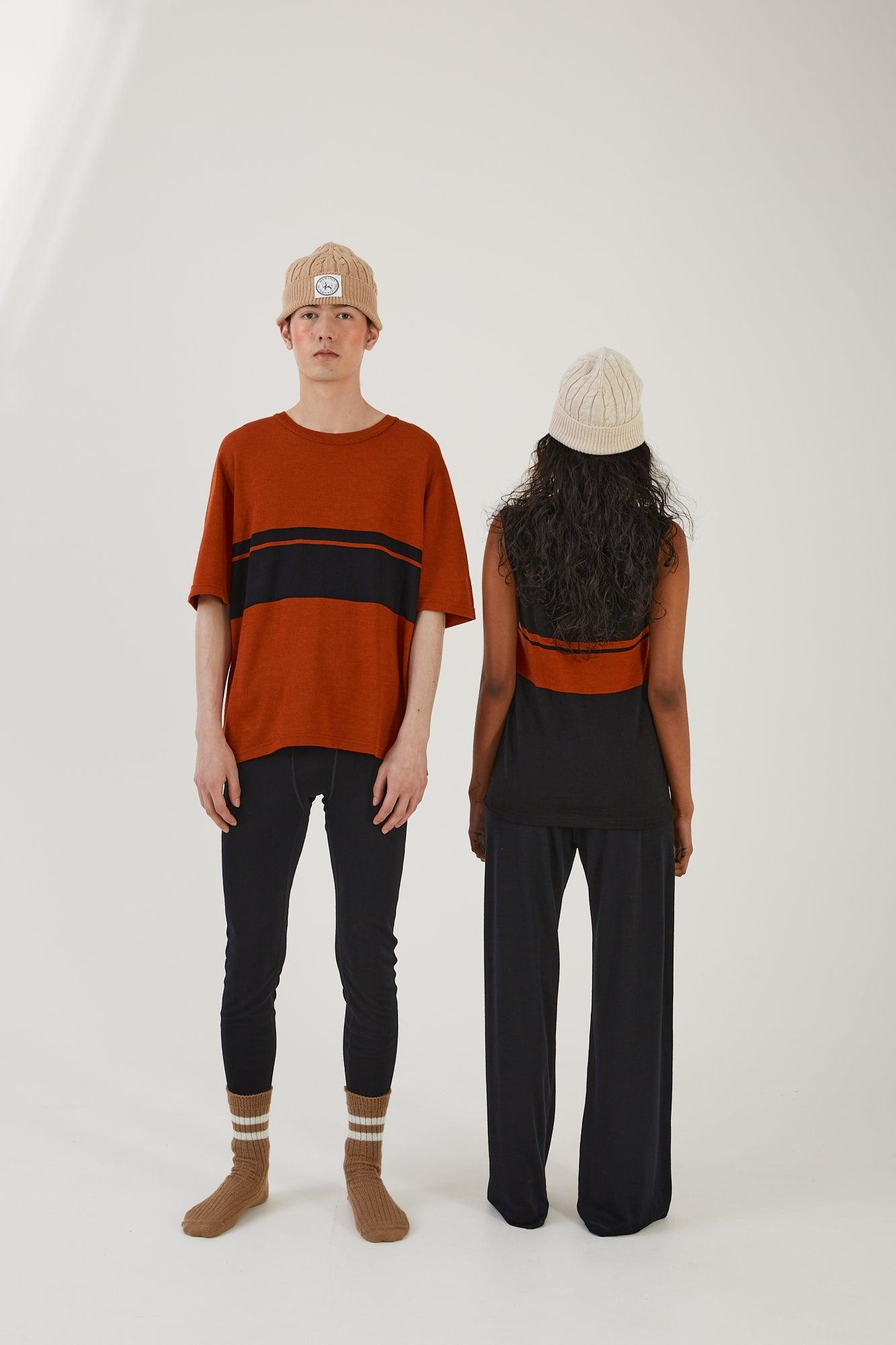 A person facing the camera wearing merino wool socks, merino wool leggings, a merino wool top and a merino wool bathers next to another person wearing merino wool track pants, a merino wool vest and a merino wool beanie