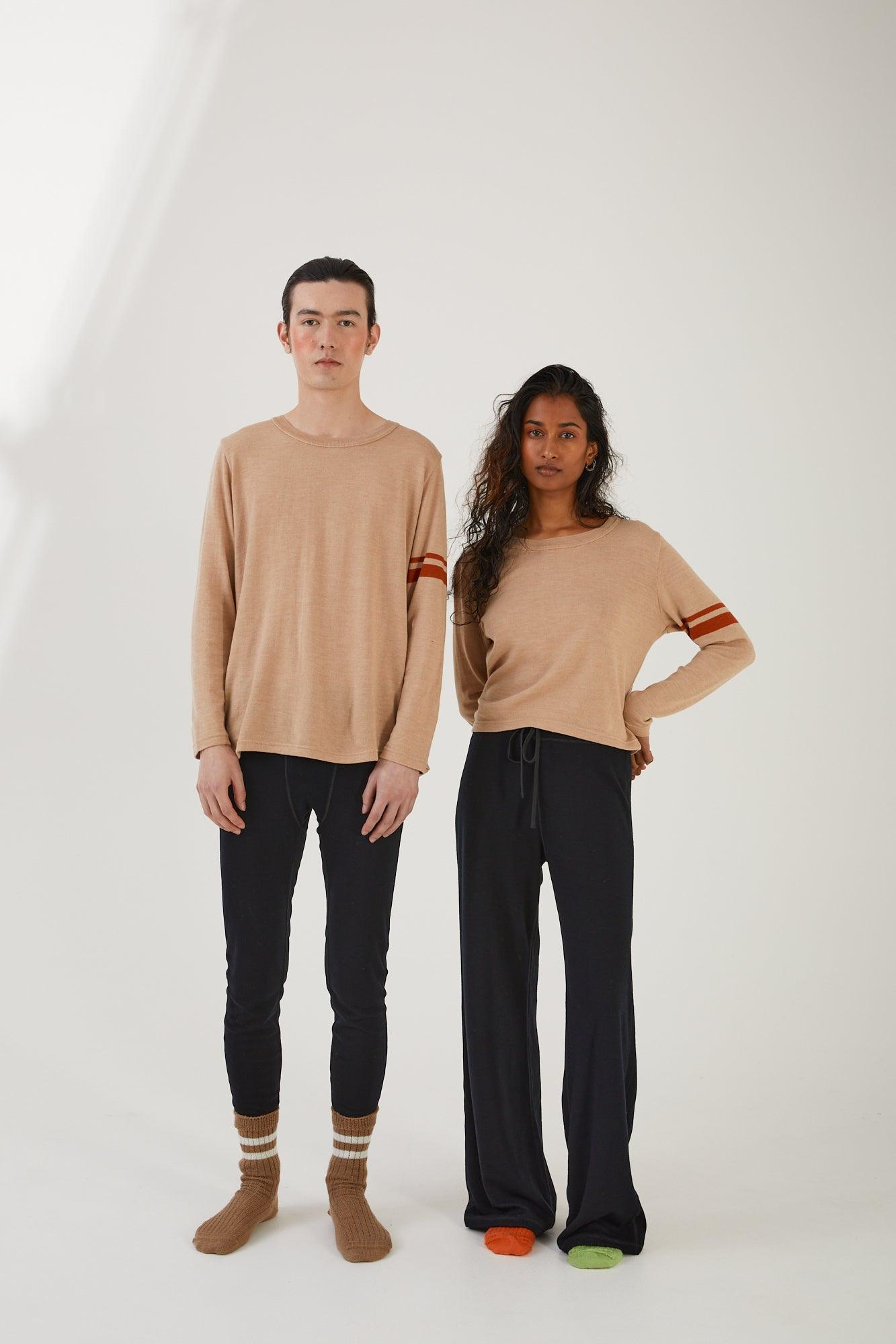 Two people facing the camera, one wearing merino wool socks, merino wool leggings and a merino wool jumper whilst the other wears merino wool socks, merino wool track pants and a merino wool sweater