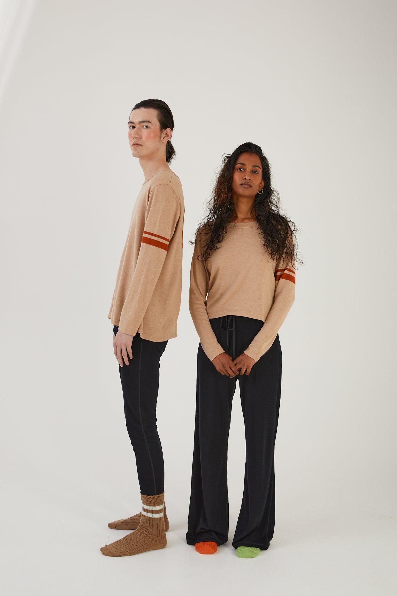 A person standing side on wearing merino wool socks, merino wool leggings and a merino wool jumper next to another person wearing merino wool socks, merino wool track pants and a merino wool jumper