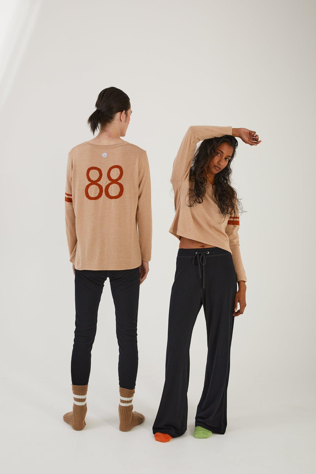 A person with their back to the camera wearing merino wool socks, merino wool leggings and a merino wool sweater next to a person facing the camera wearing merino wool socks, merino wool track pants and a merino wool jumper